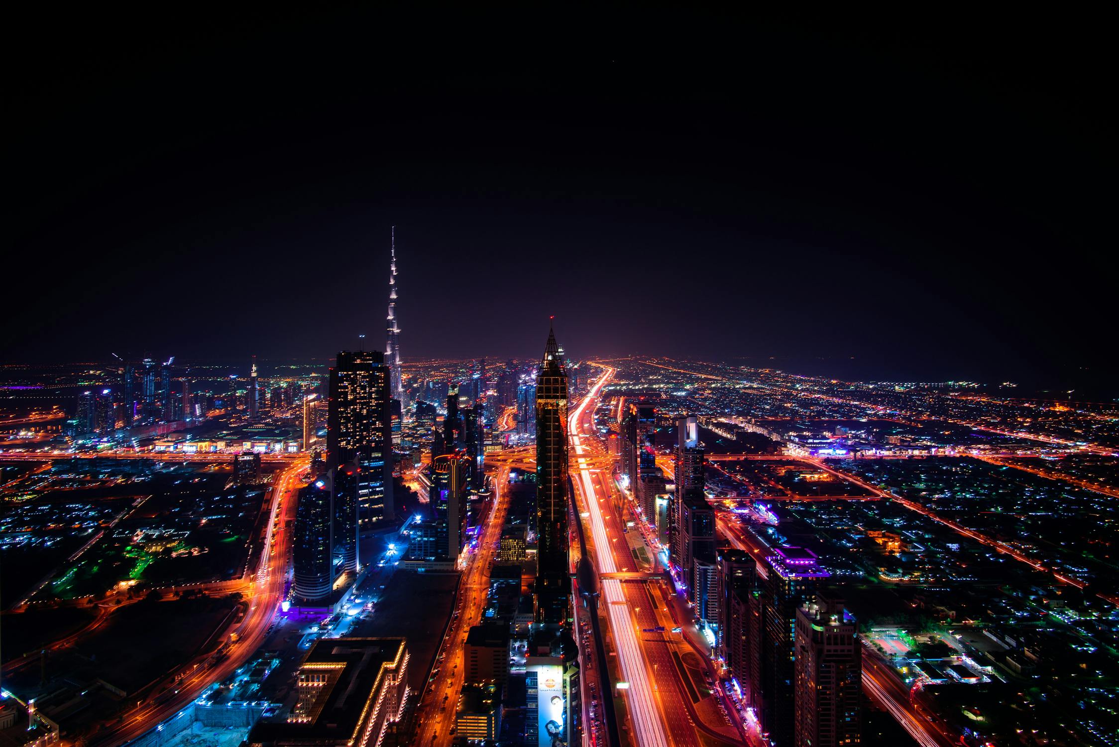 Dubai at night from above, with lit roads and towers spreading across the city.